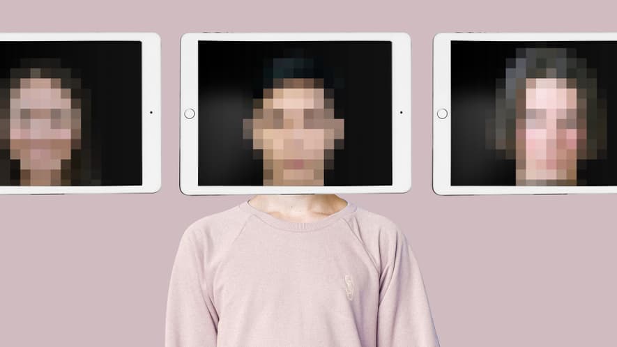 Eine Person steht vor drei Tablets, auf denen pixelige Gesichter vor einem hellrosa Hintergrund zu sehen sind.